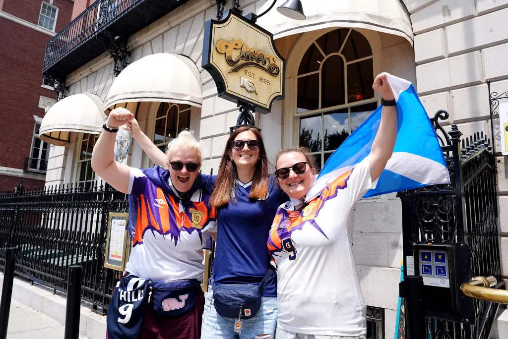 Three Scotland fans posing outside the Cheers Restaurant & Pub in Boston.
