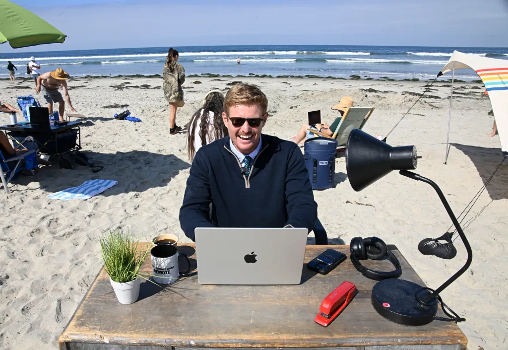 Scott Muirhead working on a laptop at a desk on the beach in San Diego.