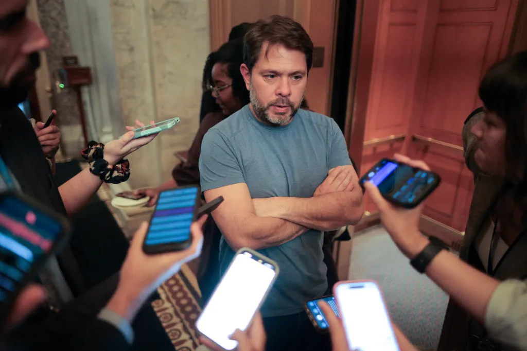 Sen. Ruben Gallego speaking to reporters holding up cell phones to record him.