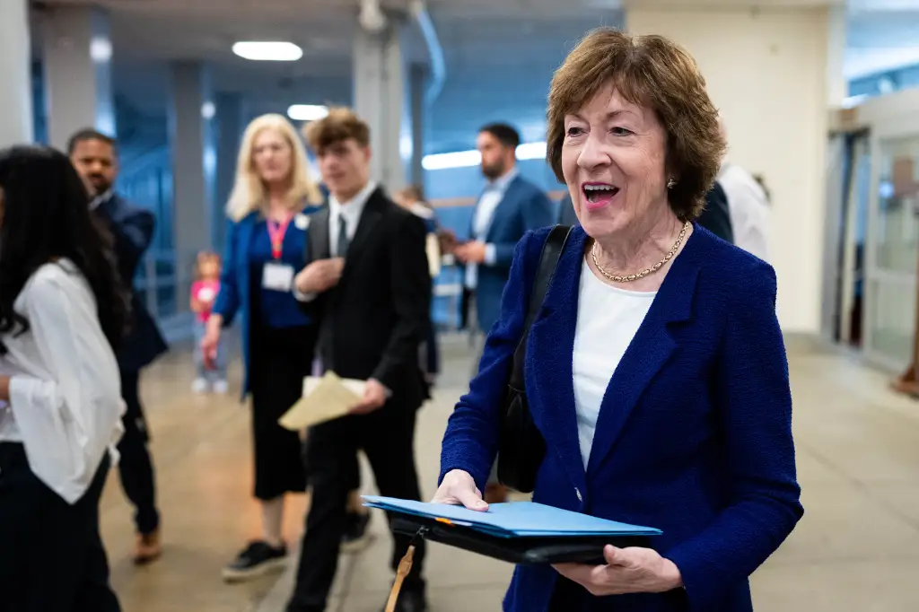Senator Susan Collins, R-Maine, smiling while holding documents and walking in the U.S. Capitol.