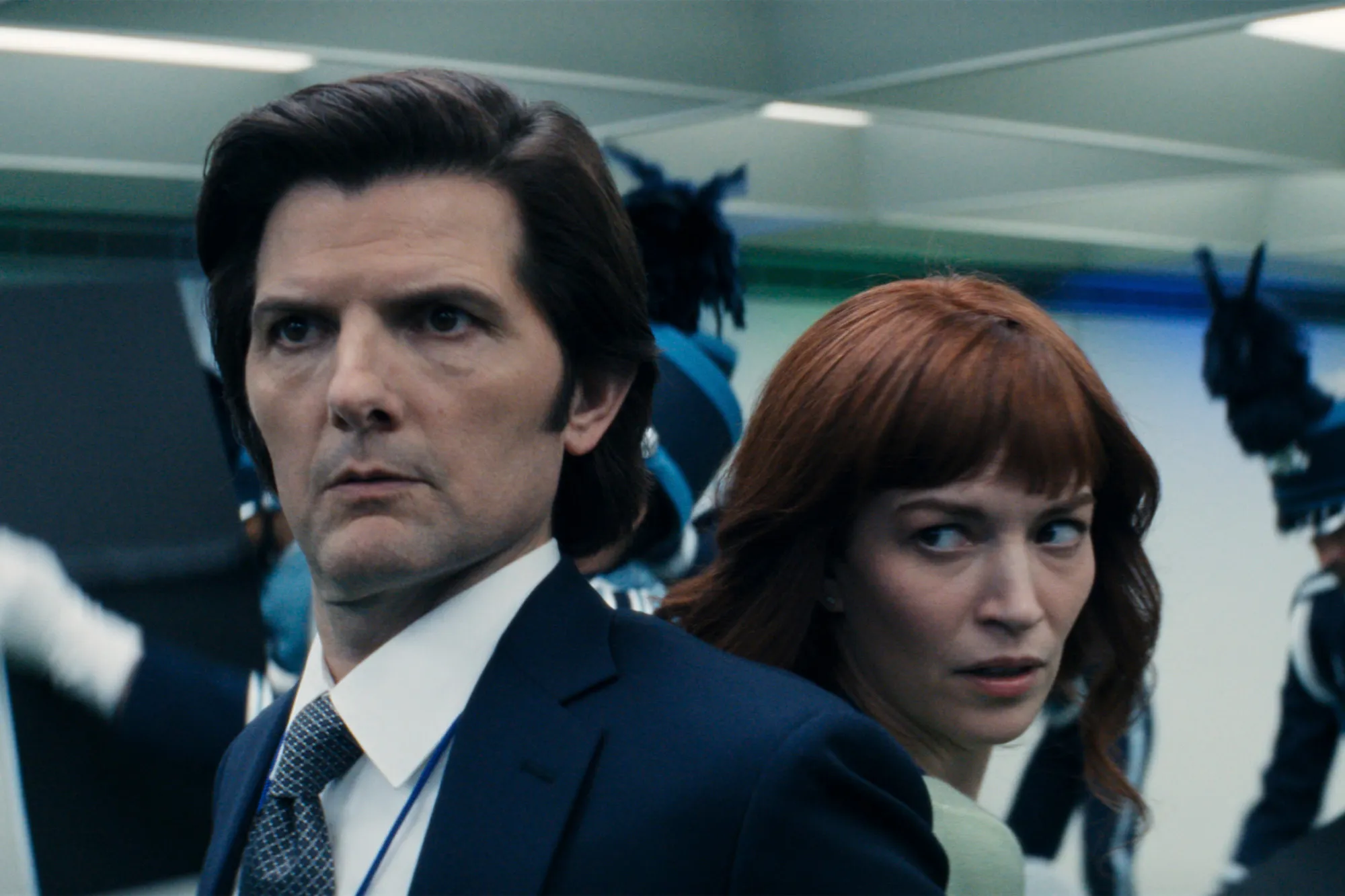 A man in a suit and a woman with red hair looking over her shoulder.