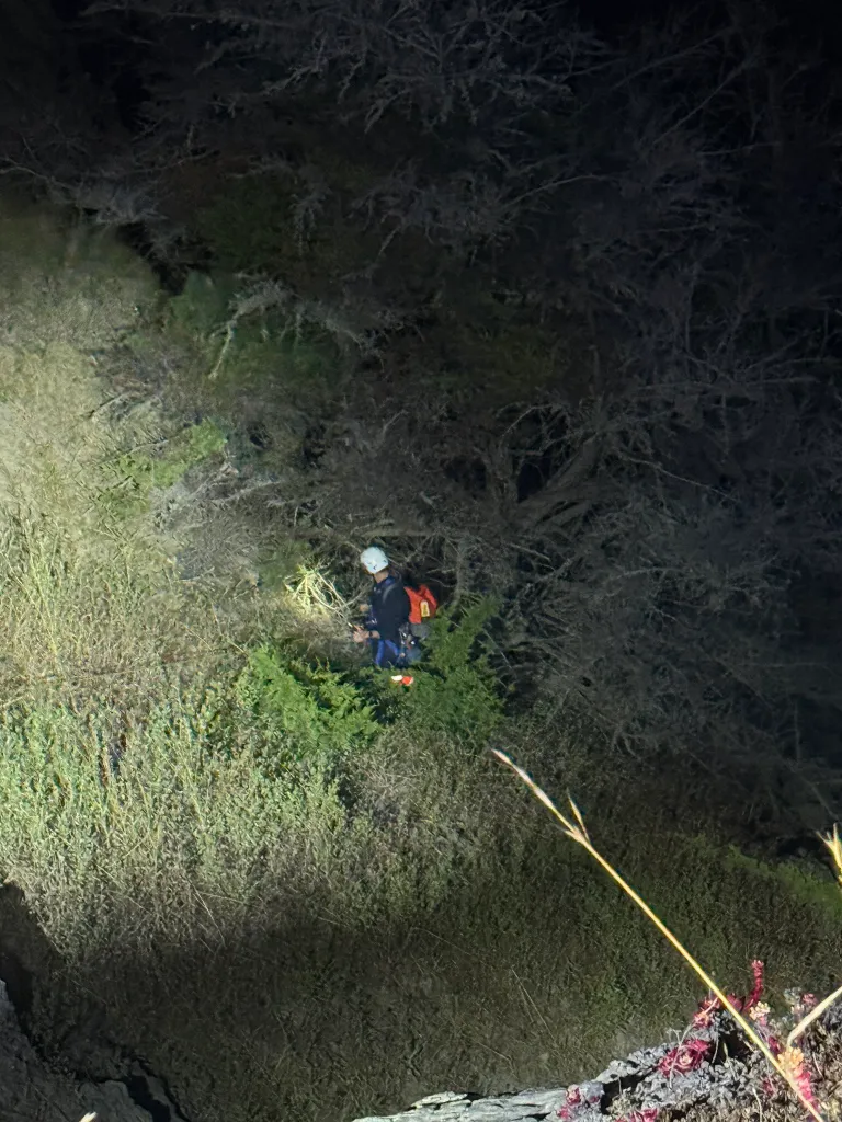 SFFD crew member with a helmet and harness in a dark, bushy area during a 7-hour rescue mission at Dead Man's Point.