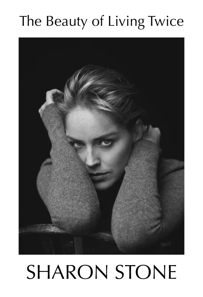 Black and white portrait of Sharon Stone looking directly at the viewer, her hands folded under her chin.