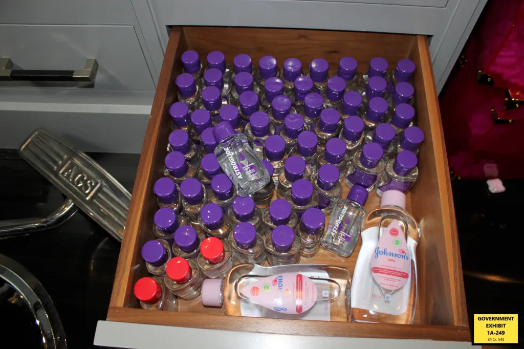 An open drawer filled with dozens of small lubricant bottles with purple caps, two larger Johnson's Baby Oil bottles, and several small lubricant bottles with red caps.
