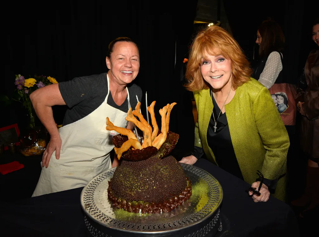 Sherry Yard and Ann-Margret next to a chocolate cake with frosting legs.