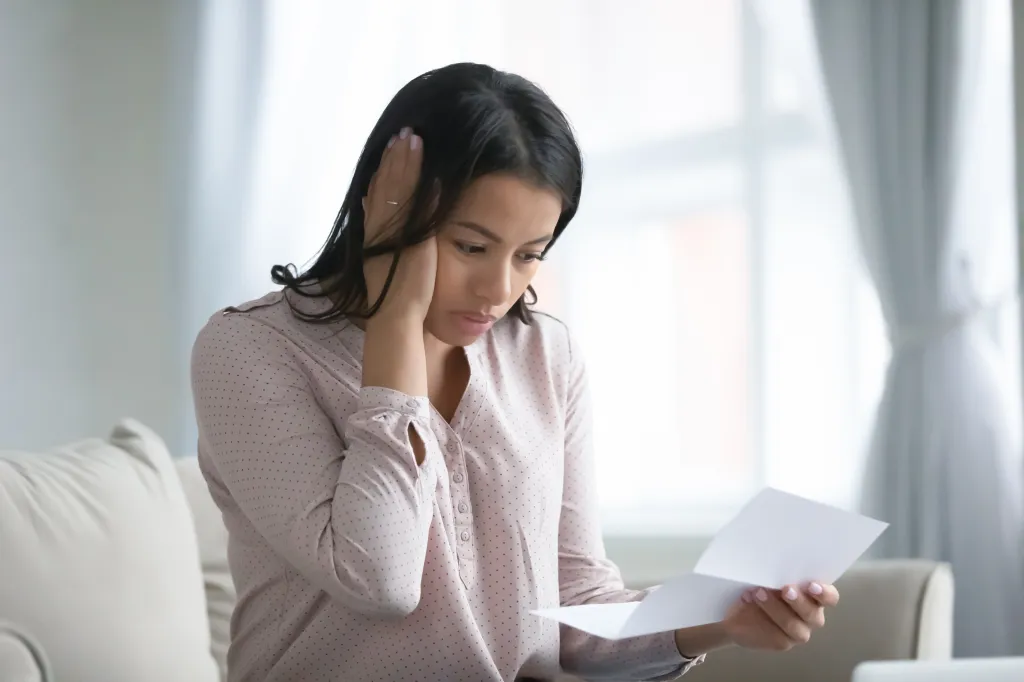 A worried woman holds a letter, receiving bad news.