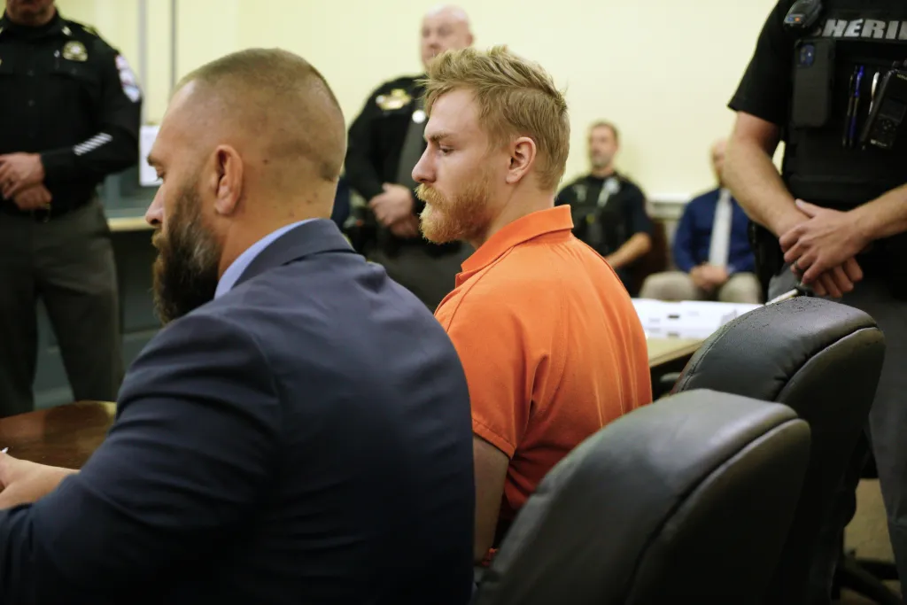 Shotsie Buck-Hayes (left) in a dark suit next to Edward Lavado (right) in an orange polo shirt during a preliminary hearing.