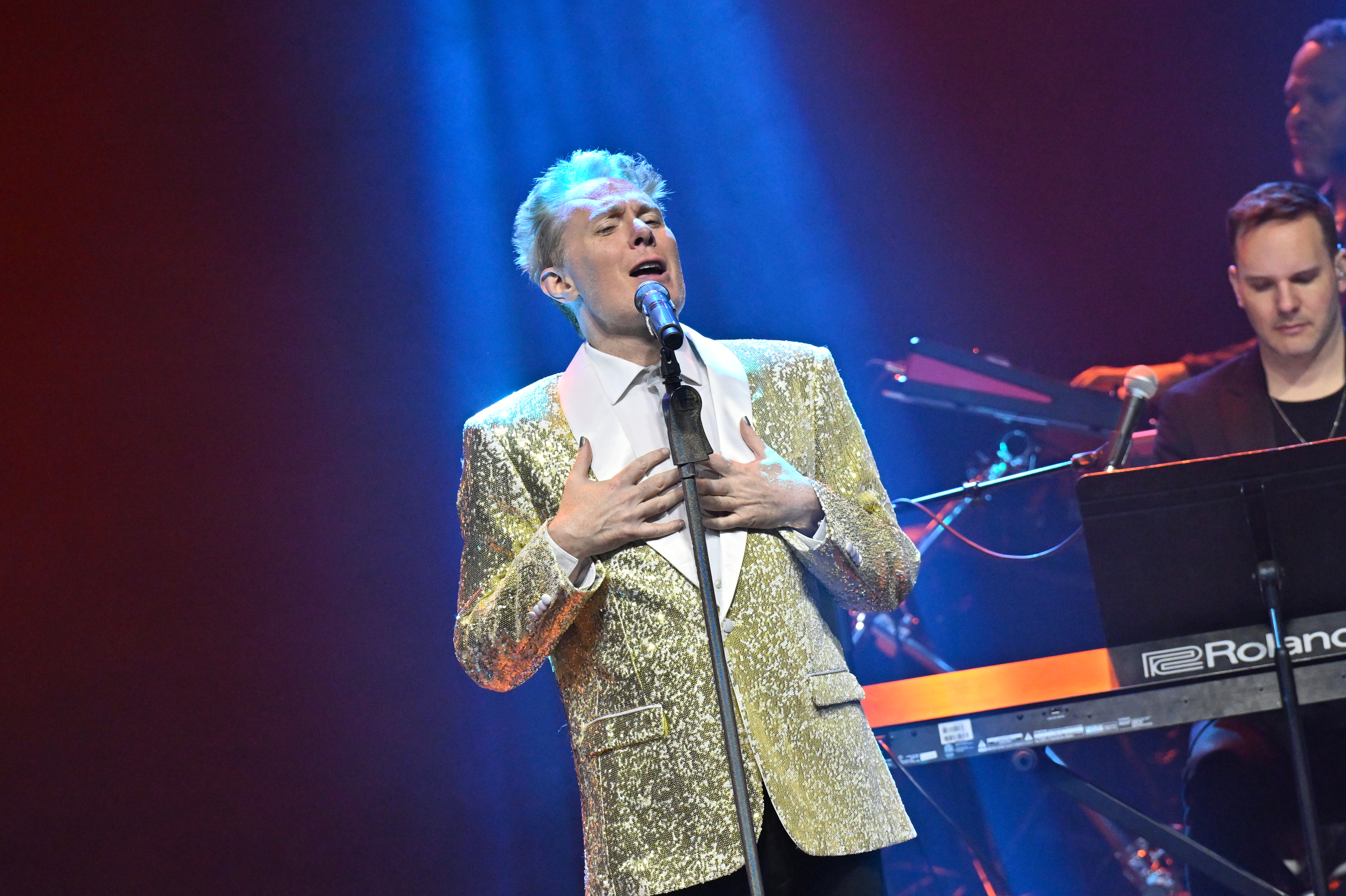 Singer Clay Aiken performs onstage in a gold sequined jacket.