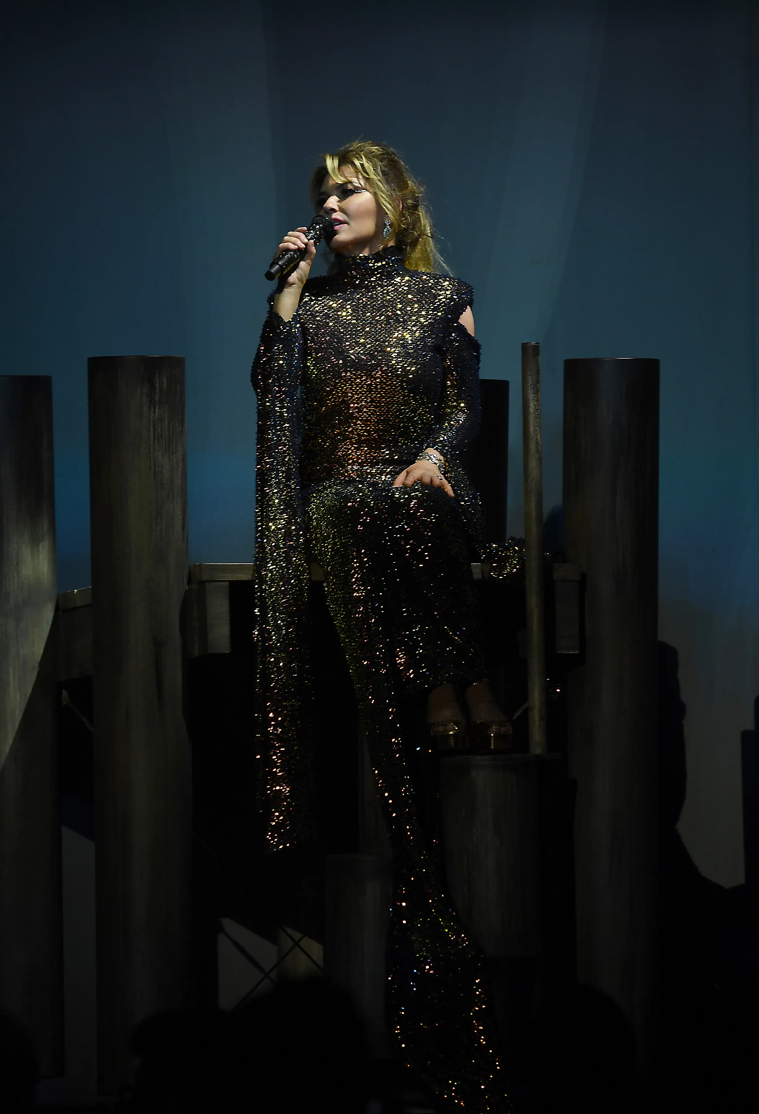 Singer Shania Twain performs in a long black sequined gown and holds a microphone.