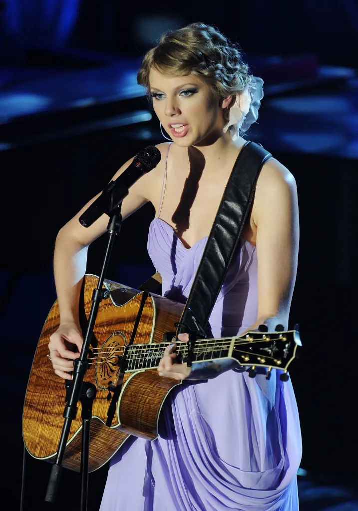 Taylor Swift performing on stage with an acoustic guitar.