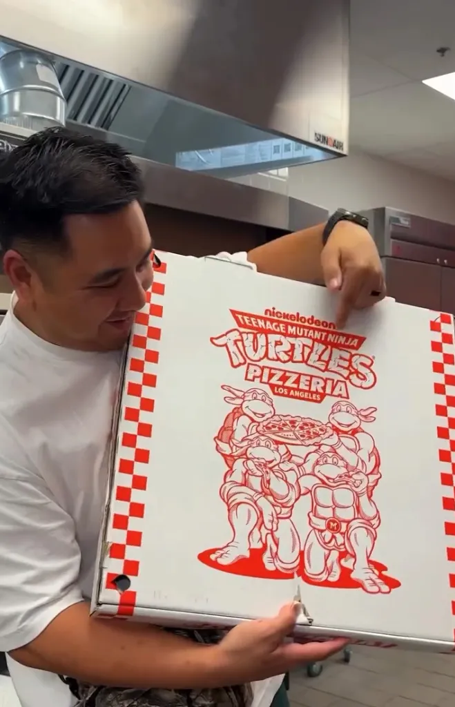 A chef holding a Teenage Mutant Ninja Turtles Pizzeria pizza box.