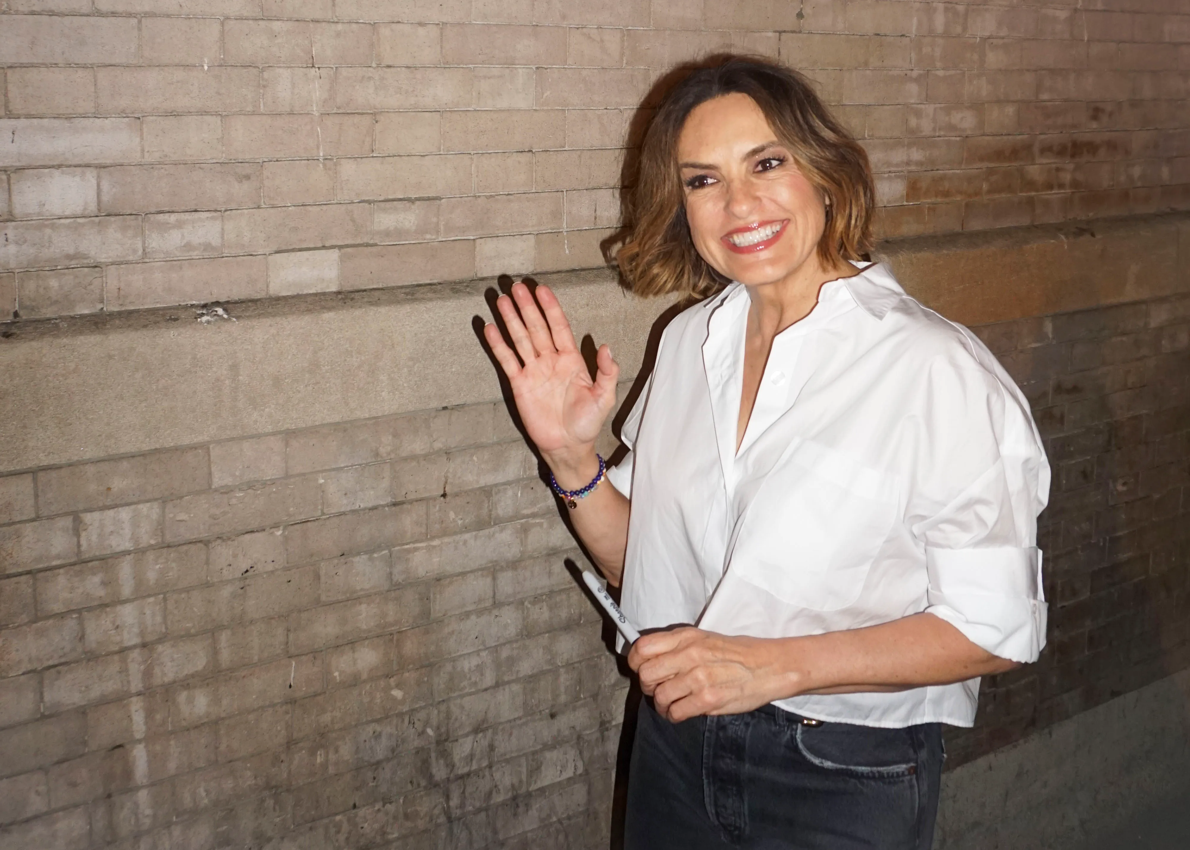 Mariska Hargitay greeting fans outside Hudson Theatre, waving with a marker in hand.