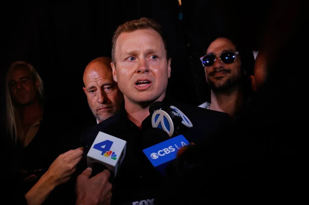 Spencer Pratt speaks into microphones from various news outlets during an election night event.