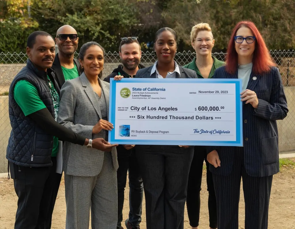 A group of seven individuals holding a large check for $600,000 for the RV Buyback & Disposal Program.