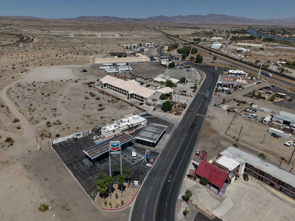 Aerial view of gas stations and motels along a highway in a desert landscape, highlighting gas price differences between California and Arizona.