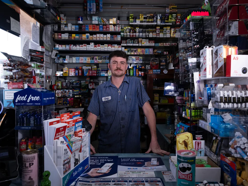 A store clerk named Cody stands behind a counter in a convenience store.