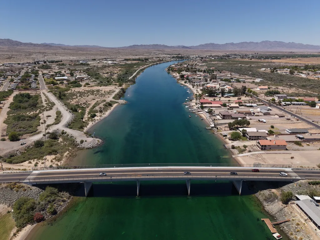Aerial view of the Colorado River, flowing through a desert landscape, with a bridge connecting the Arizona side (right) and the California side (left), where gas prices differ significantly.