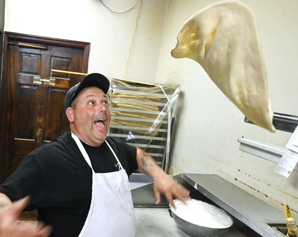 A man in a white apron throwing pizza crust in the air