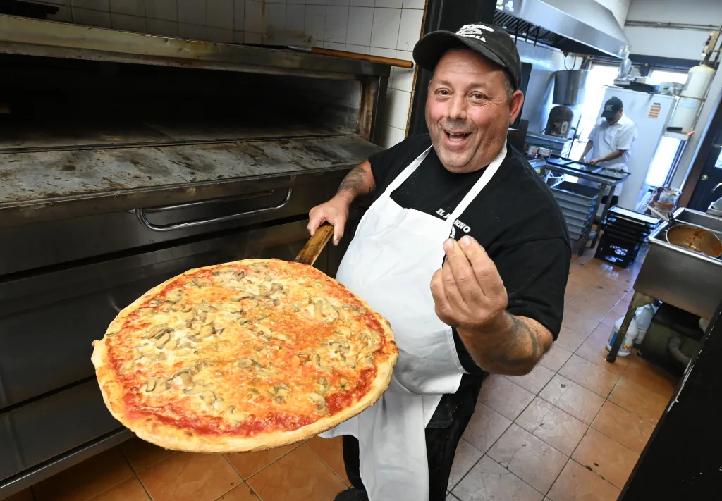 John Caggiano holding a freshly baked mushroom pizza in his pizzeria.