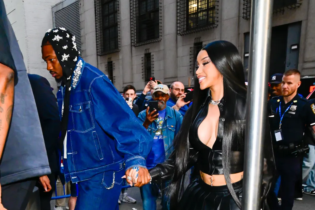 Stefon Diggs and Cardi B walking together, holding hands, with a crowd of people around them.