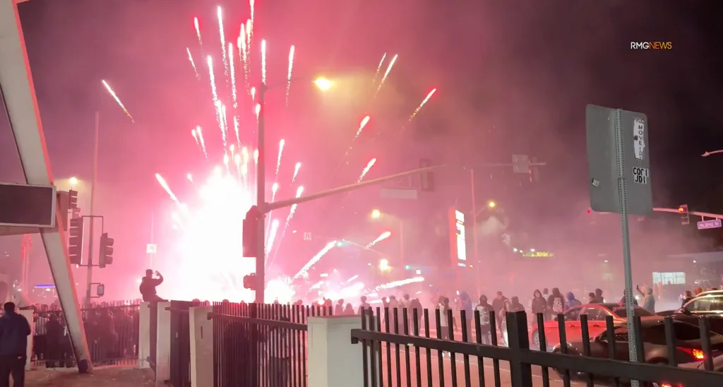 A street takeover with fireworks at night, illuminating a crowd of people and cars.
