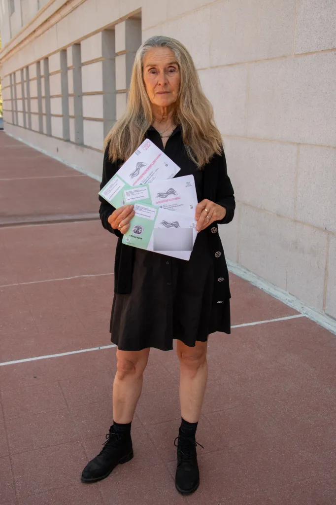 Sue Pasco displays ballots received for deceased family members outside City Hall in Los Angeles, CA.