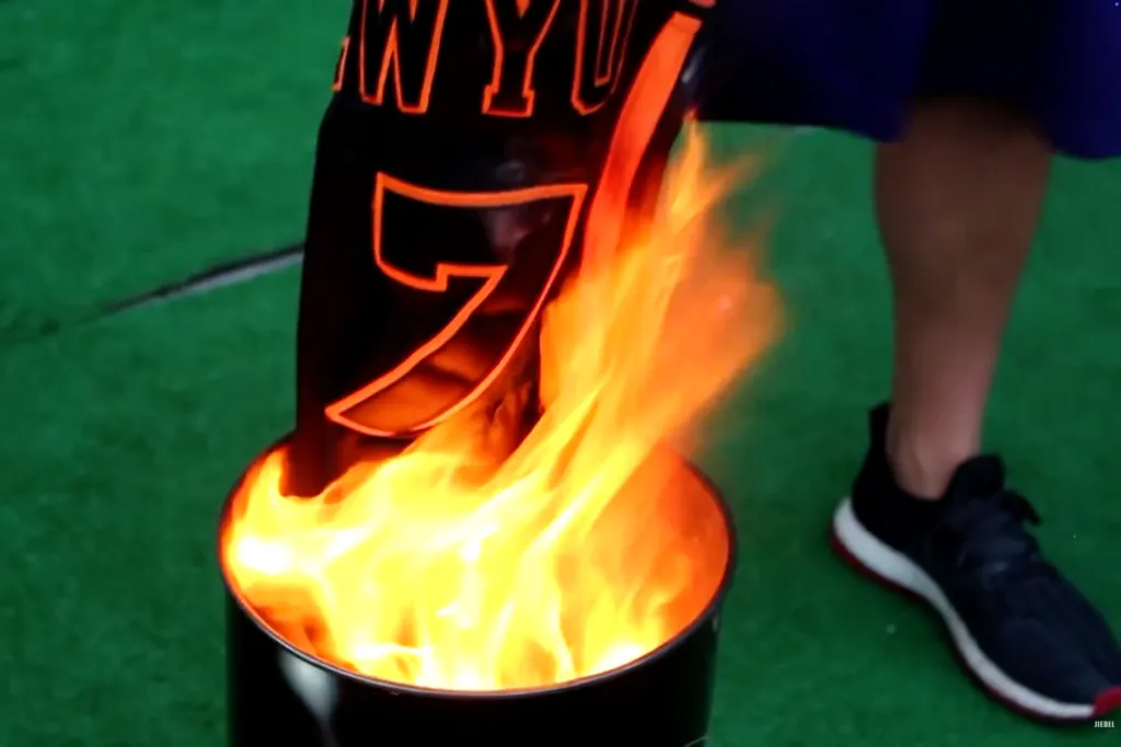 A Knicks jersey is being burned in a metal barrel.