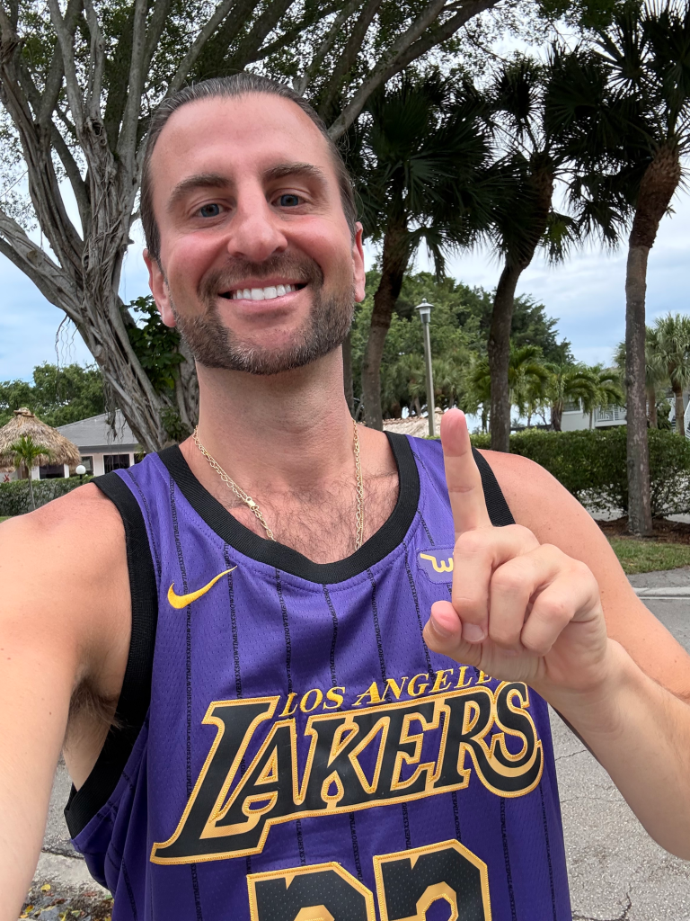 Evan Perlmutter, a lifelong Knicks fan, wears a Los Angeles Lakers jersey and smiles while giving a thumbs-up.