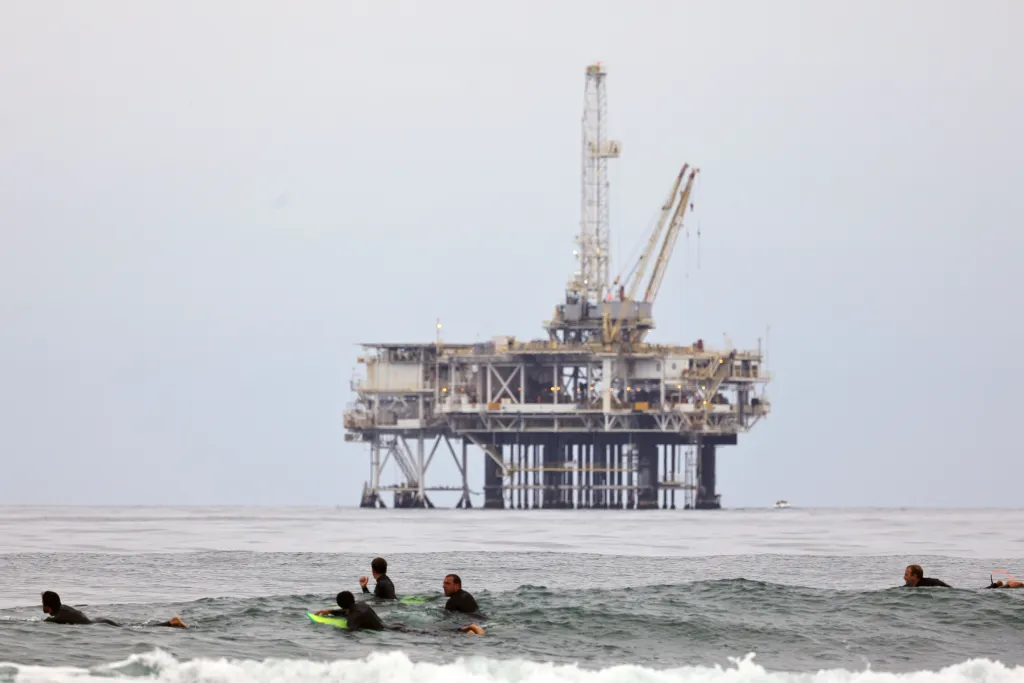 Surfers in the ocean with an oil rig in the background.