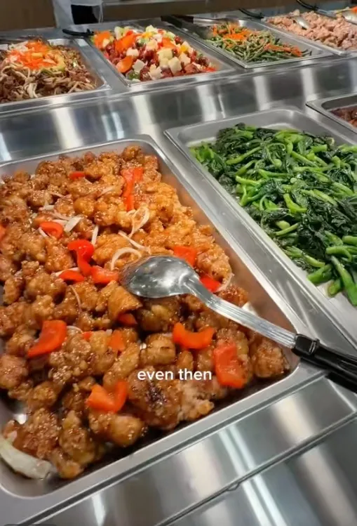 Buffet trays at T&T Supermarket with various dishes including General Tso's chicken, a vegetable dish, and noodles.