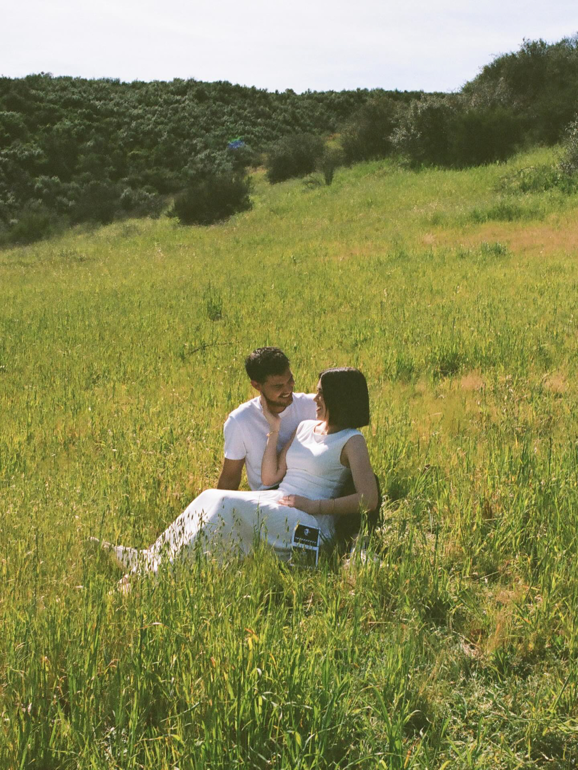 Taylor Lautner and his wife Taylor Dome sitting in a grassy field, with a sonogram photo in her lap.