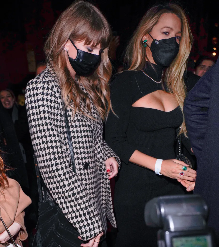 Taylor Swift in a black and white houndstooth coat and Blake Lively in a black dress, both wearing black masks.