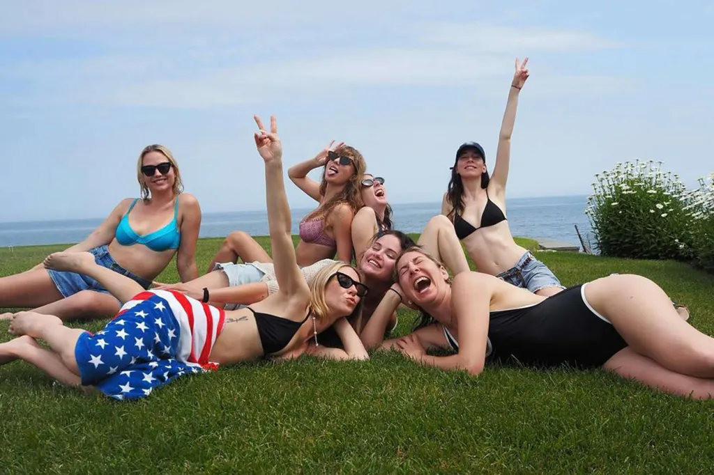 Taylor Swift and Selena Gomez posing in bikinis on the grass with friends.
