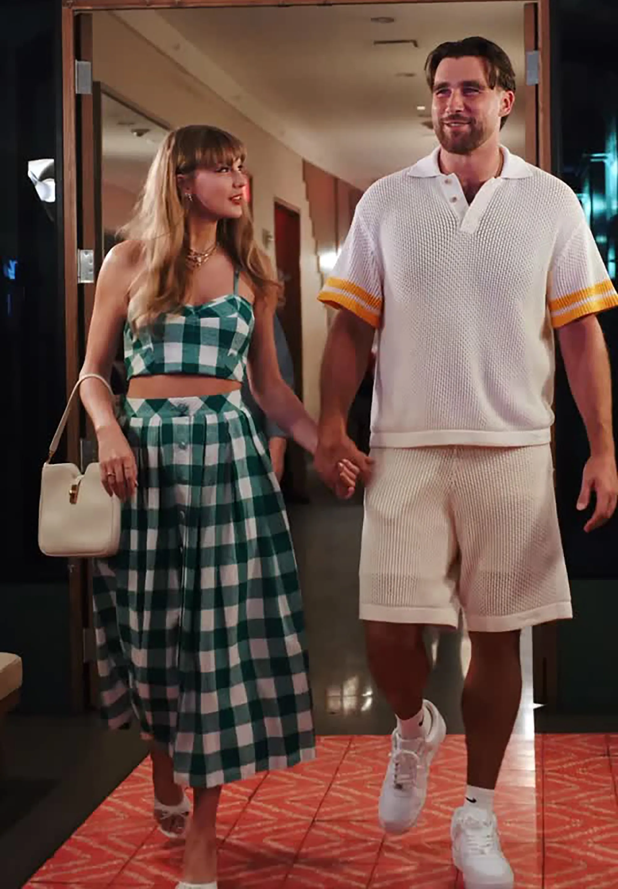 Taylor Swift in a green and white plaid dress, holding hands with Travis Kelce in a white polo and white shorts.