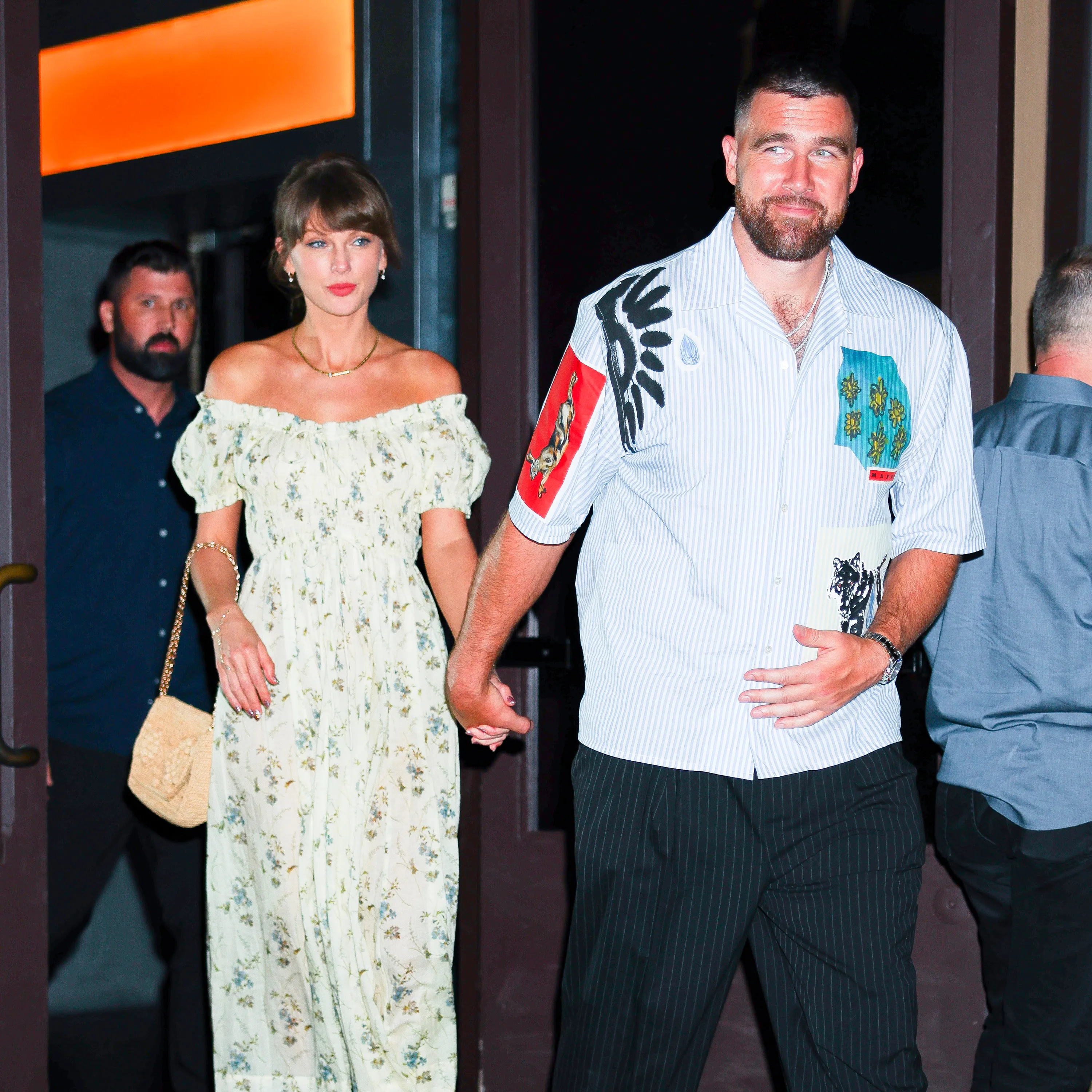 Taylor Swift and Travis Kelce holding hands while leaving a building.