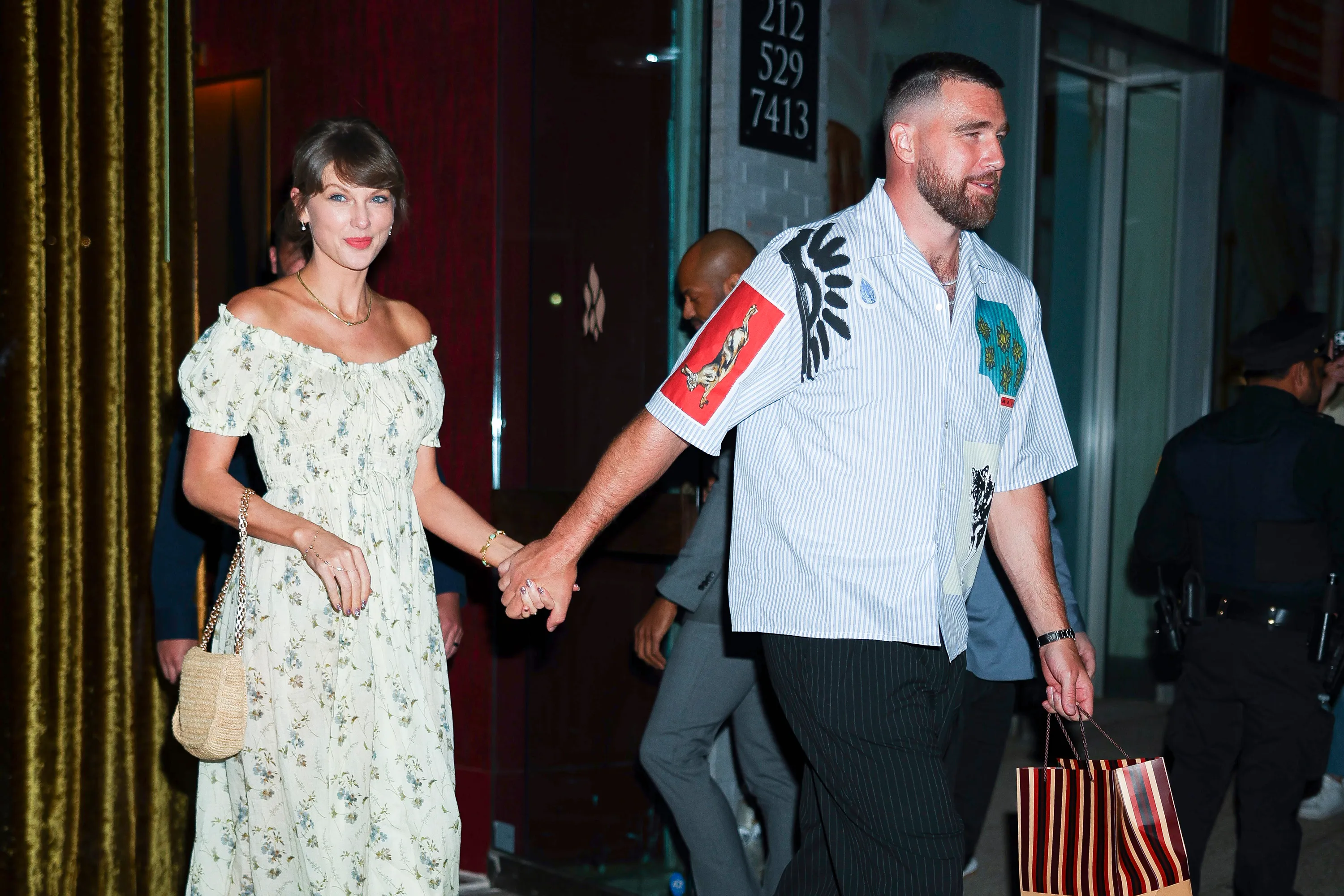 Taylor Swift and Travis Kelce holding hands while leaving a building.
