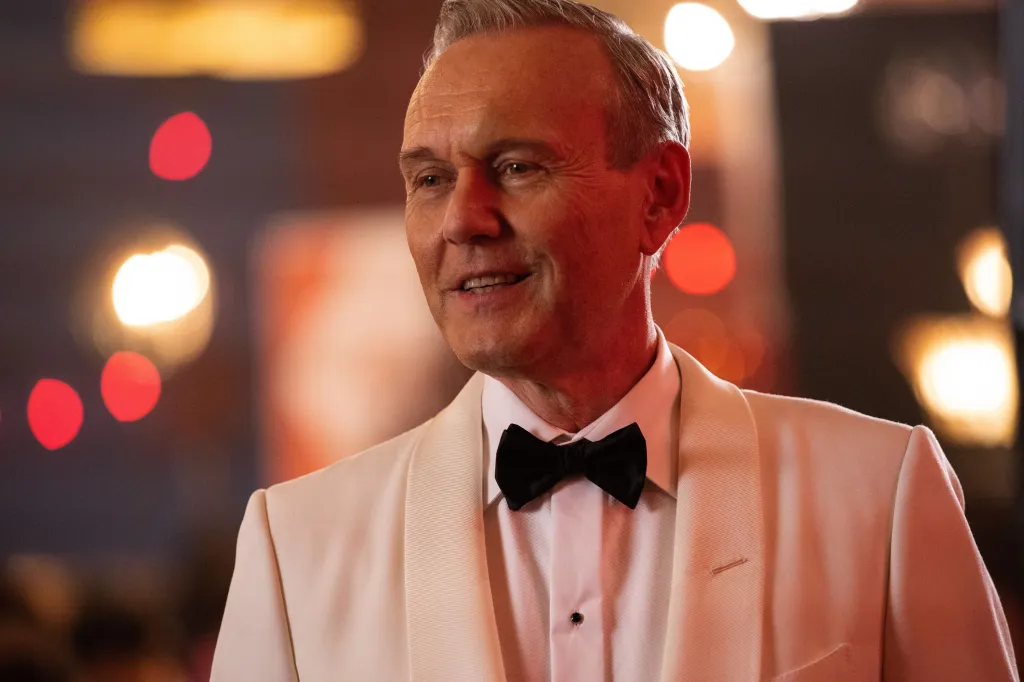 Anthony Stewart Head in a light-colored tuxedo and black bow tie, smiling.