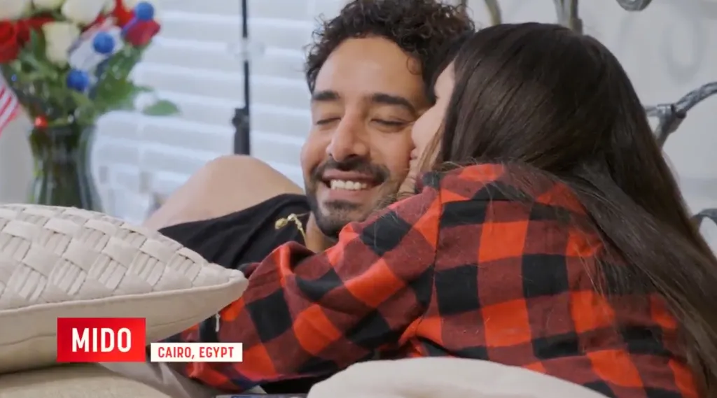 Mido and Debby lying in bed, with Debby resting her head on Mido's shoulder.