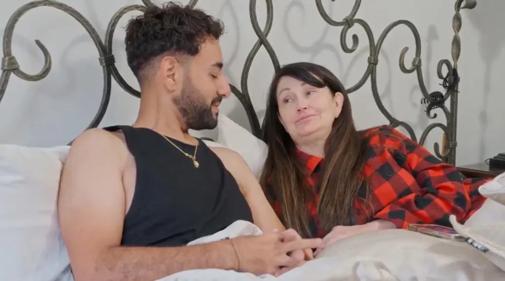 Mido and Debby lying in bed, looking at each other, with Debby smiling slightly.