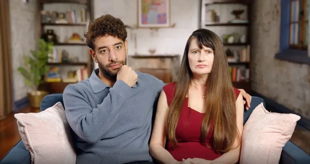 Mido and Debby looking serious on a couch, with Mido resting his hand on his chin.