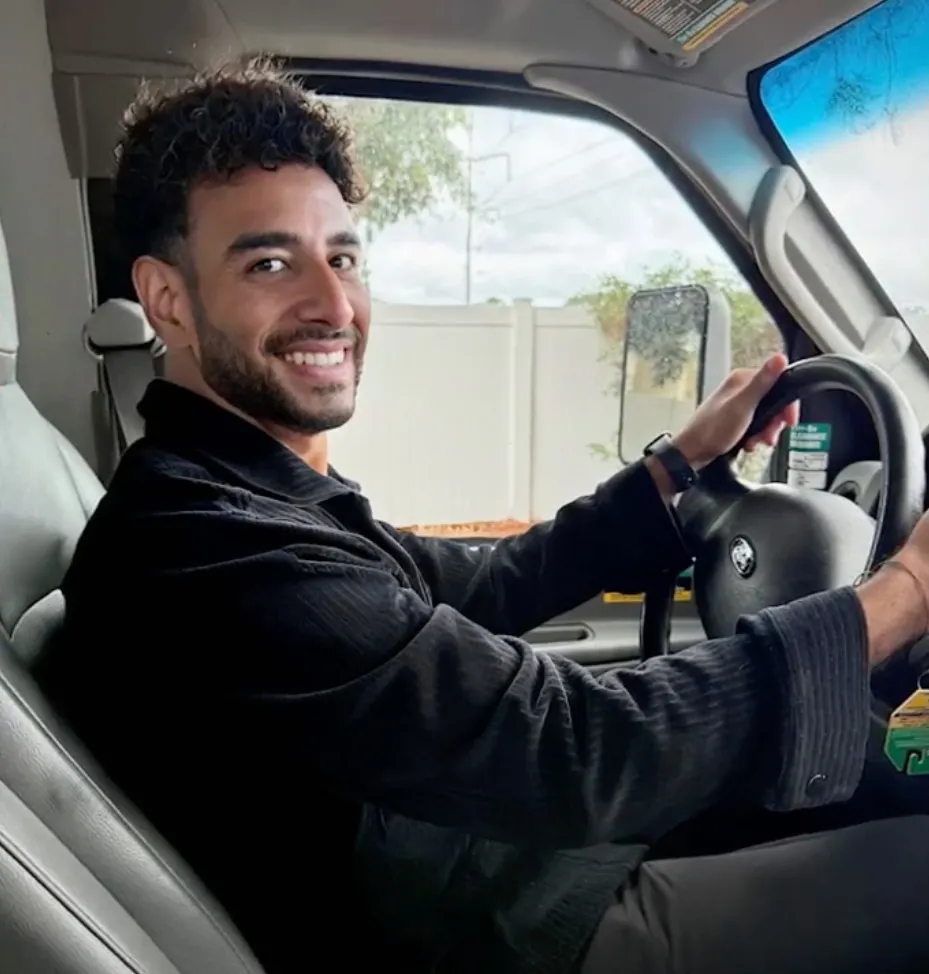 Mido, from 90 Day Fiance, smiles while sitting in the driver's seat of a vehicle.