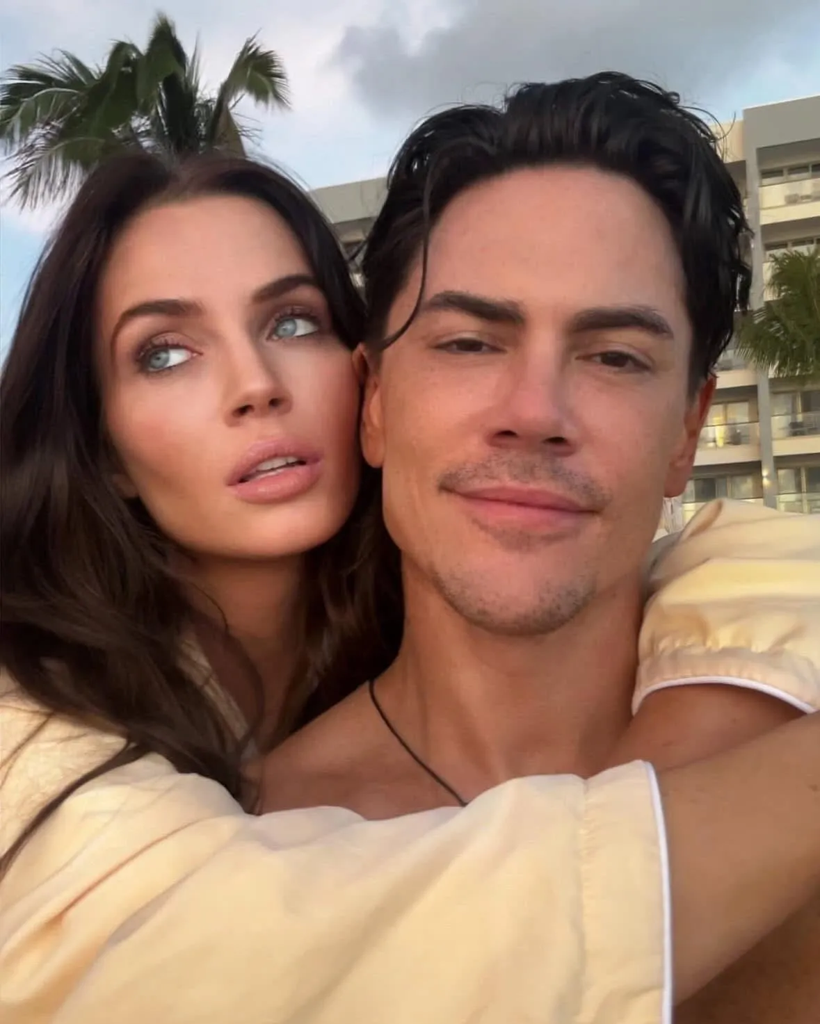 Tom Sandoval and Victoria Lee Robinson posing together, with a building and palm tree in the background.