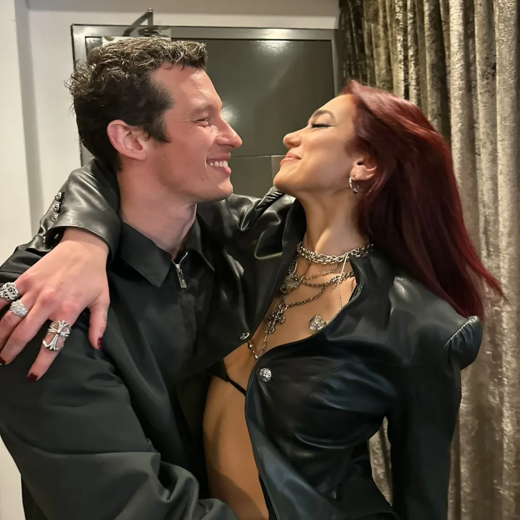 Dua Lipa and Callum Turner embracing and smiling at each other.