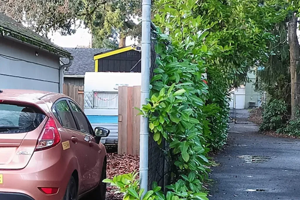 Top of a tiny home, black with yellow trim, parked behind a car and trailer in a driveway.