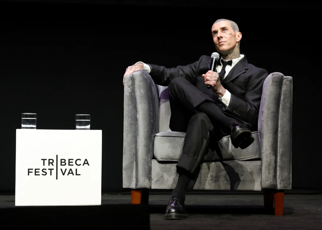 Travis Barker, seated and holding a microphone, speaks at the 