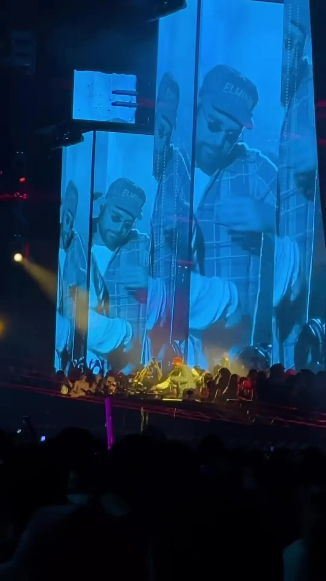 A live concert showing Travis Kelce dancing on stage, with large screens behind him displaying his image.