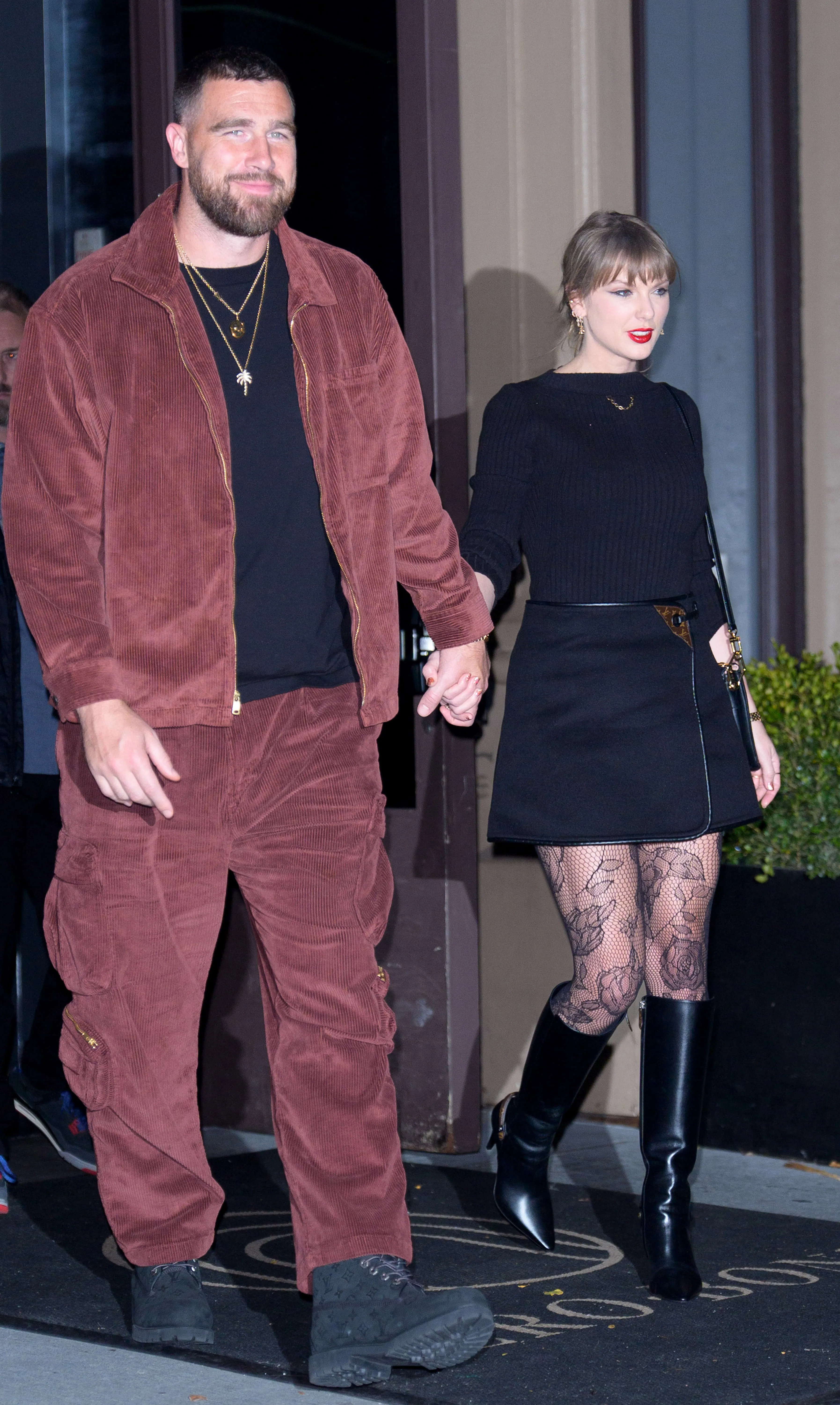 Travis Kelce and Taylor Swift holding hands while walking out of a building.