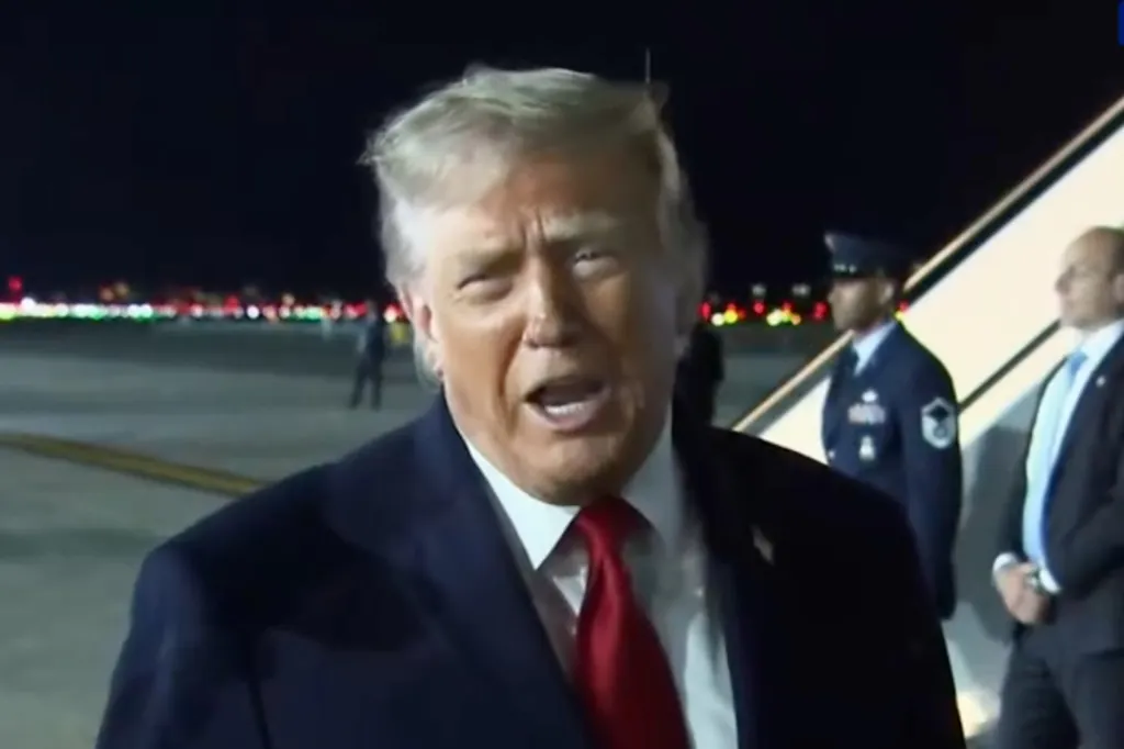 Donald Trump speaking outdoors at night, with two men in uniform standing behind him.