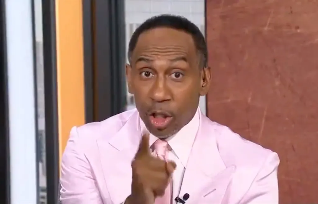 Stephen A. Smith wearing a light pink suit and tie, pointing forward with an open mouth expression.