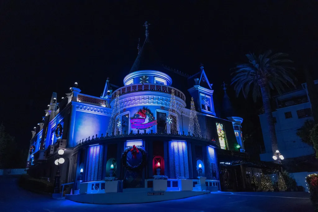 The Magic Castle, a mansion in Los Angeles, decorated with blue lights, wreaths, and Christmas trees at night.